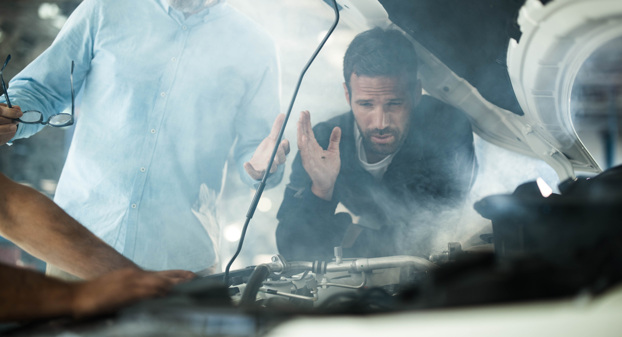 A car owner and buyers looking into the smoking engine compartment of a car.