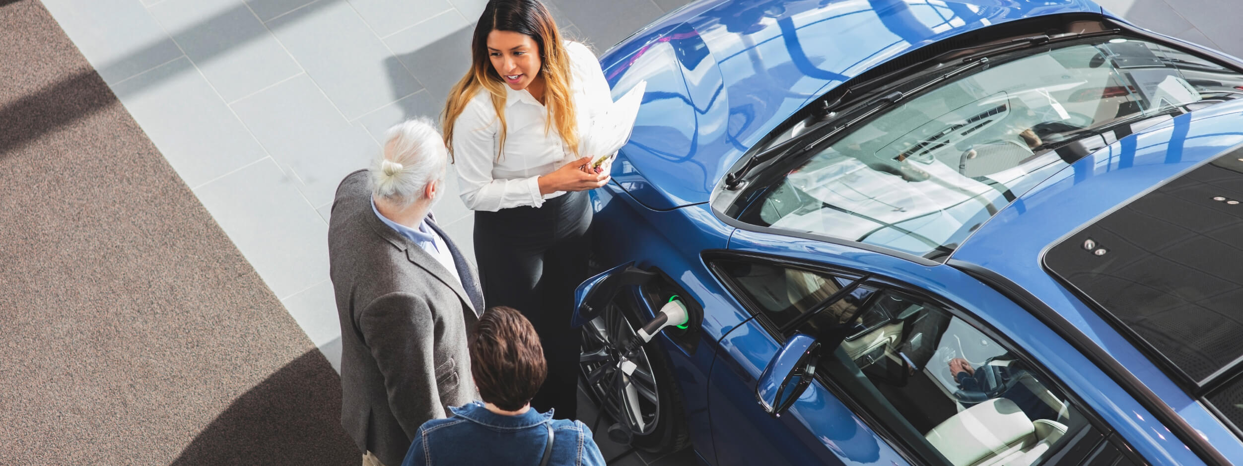 Two car shoppers standing next to an EV, talking to a salesperson.