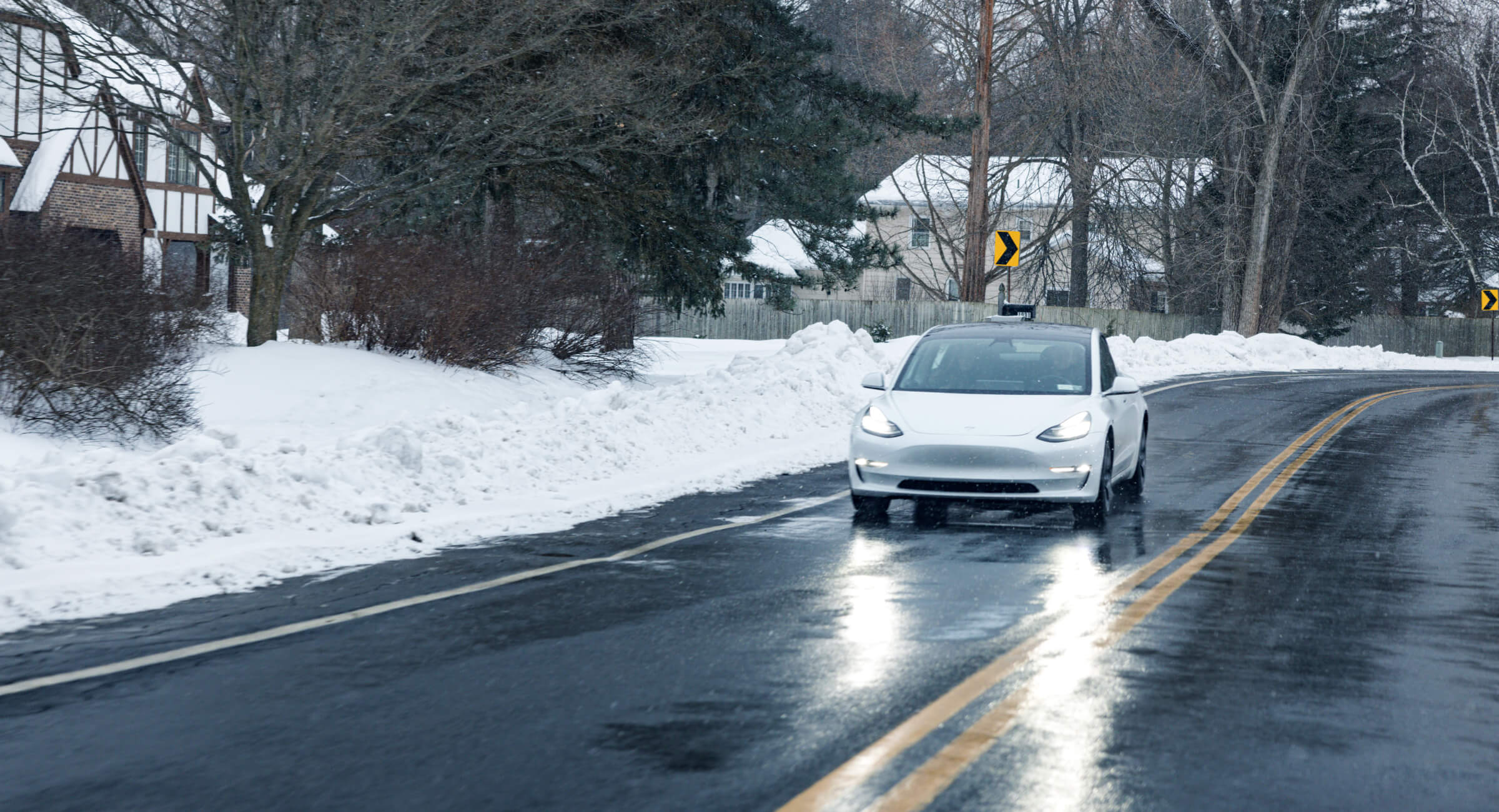 An electric car drives through a snowy neighborhood.