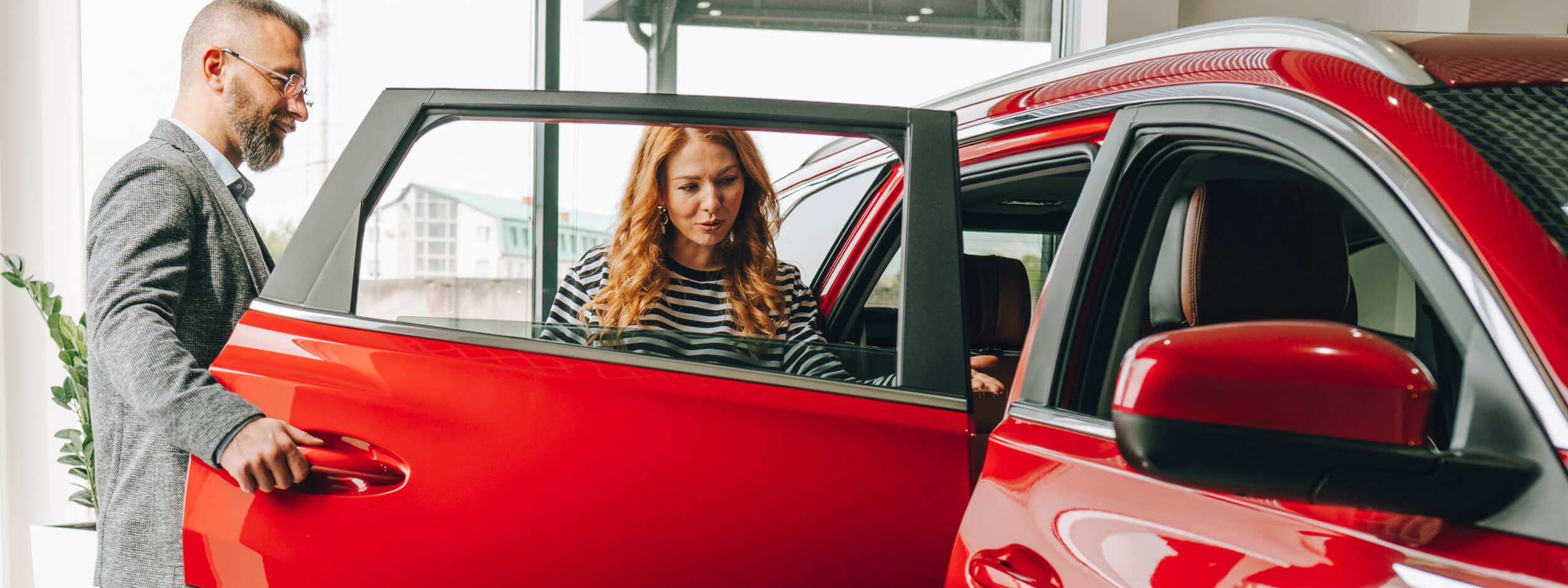 A woman looks at a hybrid vehicle in a showroom, while a salesman looks on.