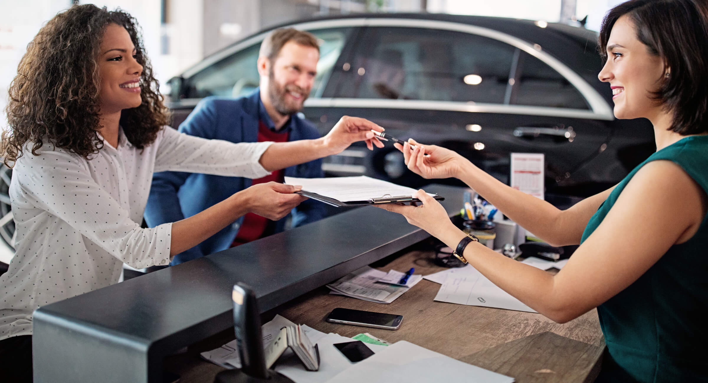 A woman hands over completed paperwork for her vehicle trade-in at a car dealership.