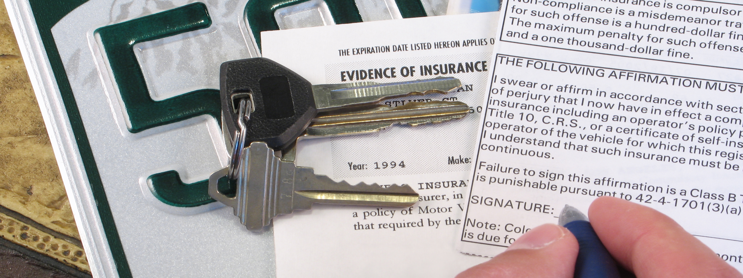 Close-up of a vehicle's title document, license plate, and keys, with a hand holding a pen ready to sign.