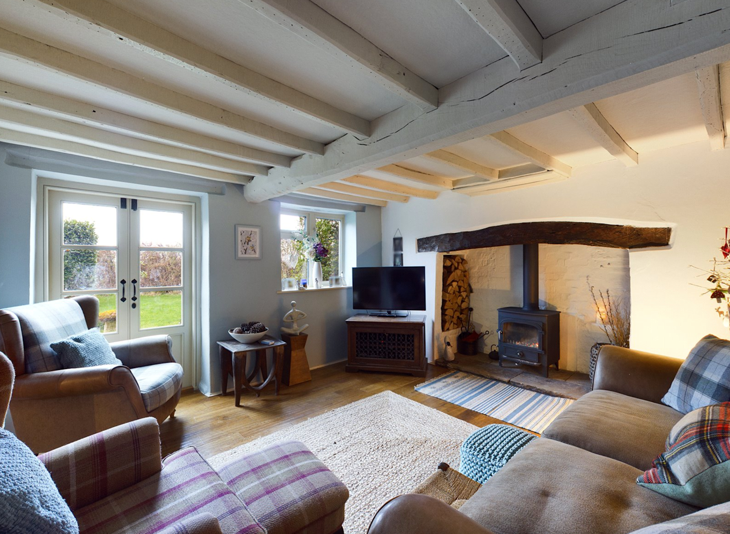 Inside the living of an old timber framed cottage with exposed beams, lots of sofas and a wood fire