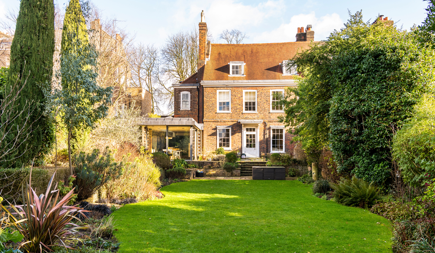 Stunning period family home with a pitched red tile roof and original sash windows, plus a modern dining extension leading out into lawned garden with mature shrubs
