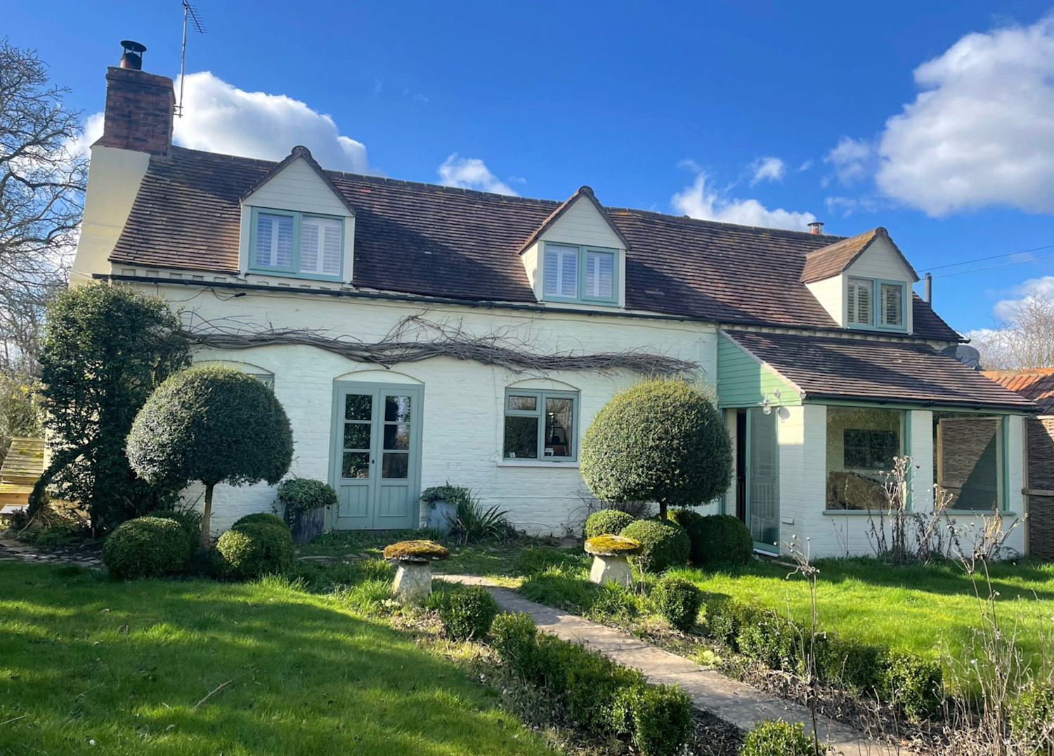 Cute period cottage with gabled roof and red tiles surrounded by pretty gardens