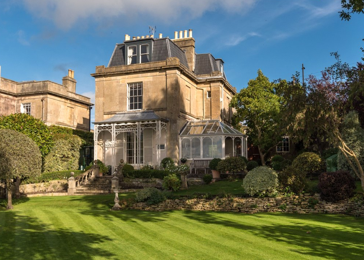 Detached Regency-style home in pale stone with decorative wrought iron porch and conservatory