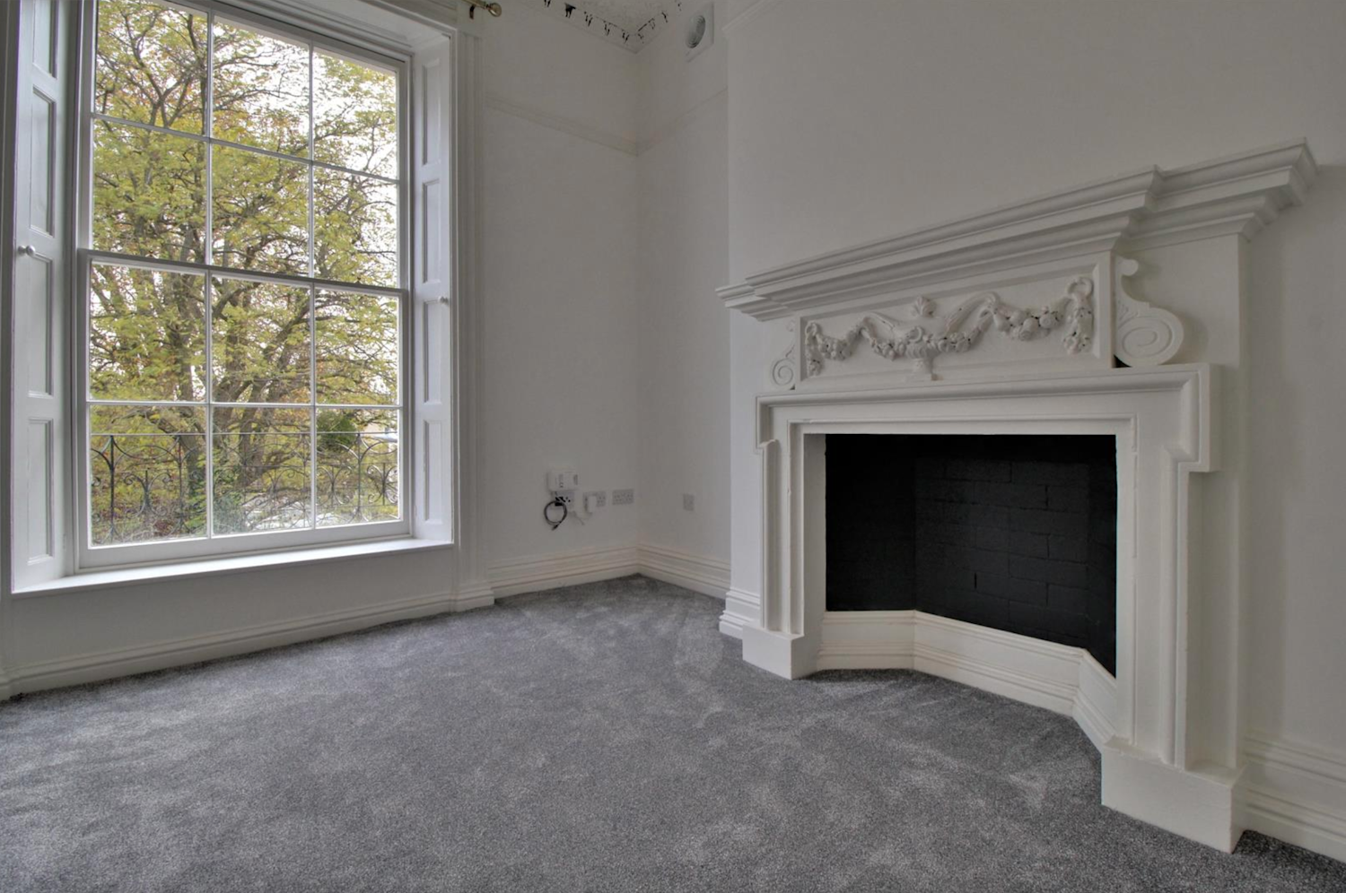 Georgian-era living room with an original fireplace and windows plus new grey carpet and white walls