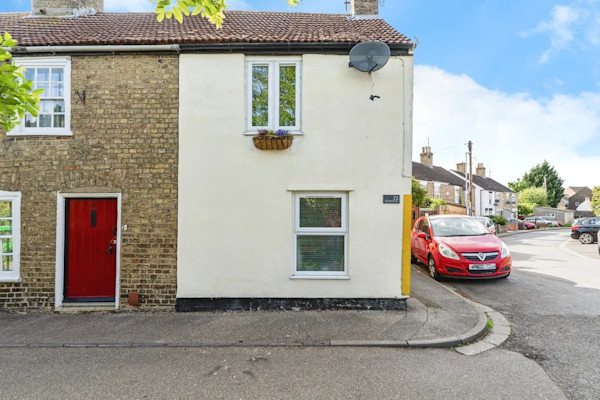 The exterior of a simple end-terrace cottage for sale in March, set on the pavement and on the corner of a road