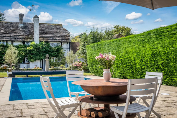 A photo taken from a patio seating area with views over a swimming pool towards an historic house