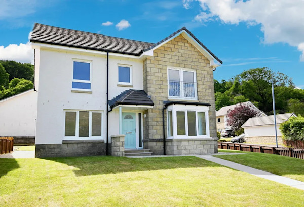 The exterior of a detached new-build family home with a neat lawn and garden path leading to the turquoise front door