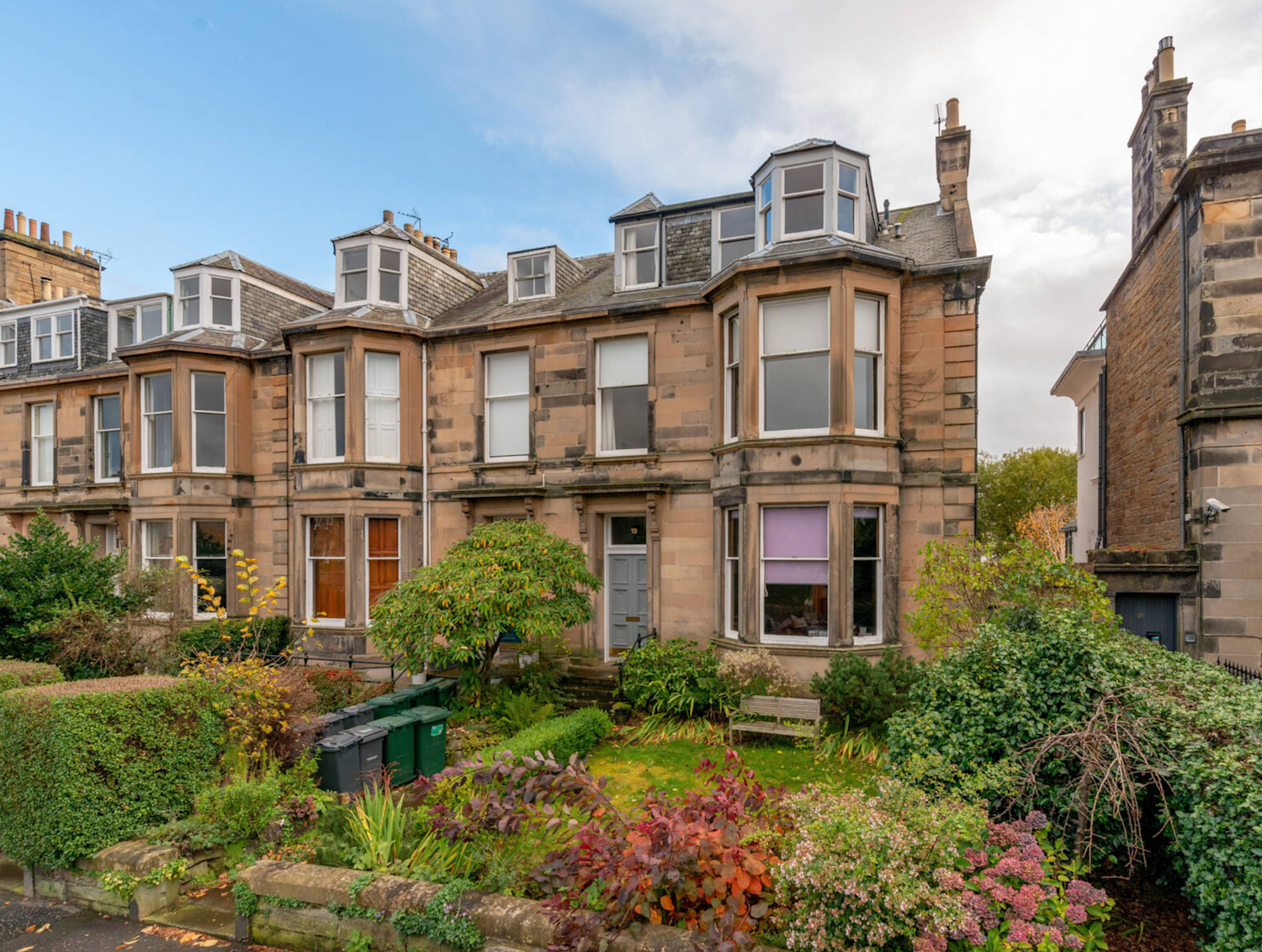 Victorian house with bay windows and a grass front garden with shrubs and bench