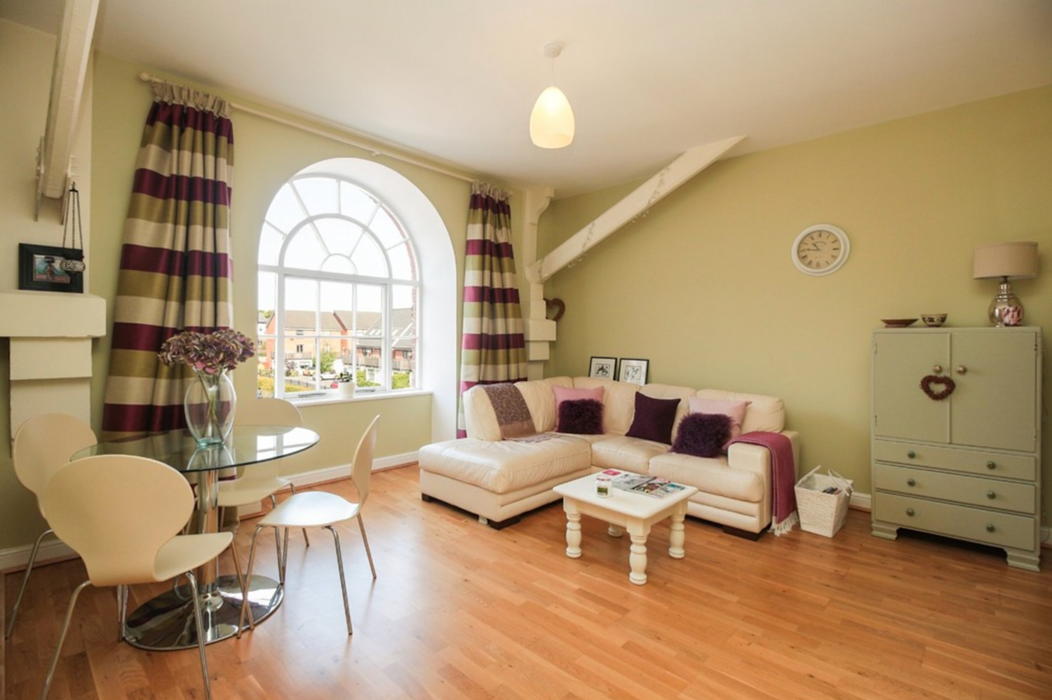 Interior of a flat with laminate flooring and pale green walls, with impressive period windows