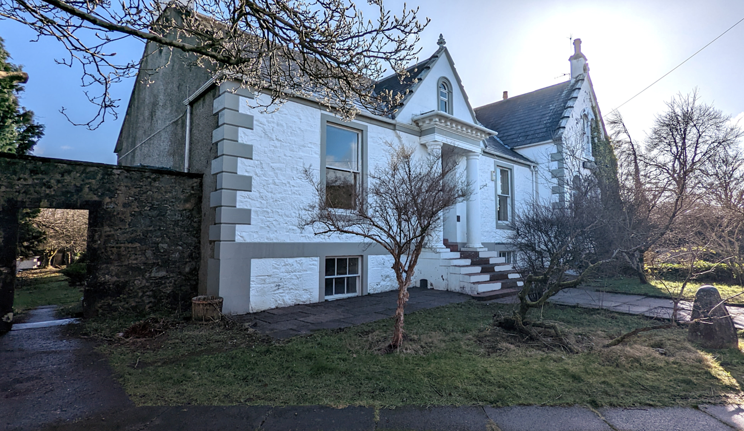 Detached white house with steps leading up to the front door, sash windows and a stone archway at the side for access to the gardens