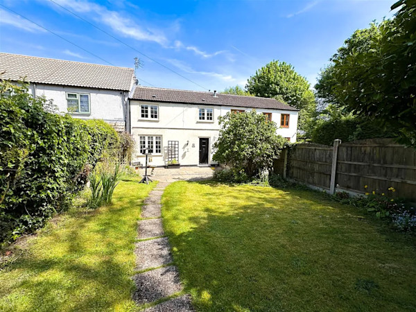 The exterior of a white terraced cottage set behind a large lawned garden