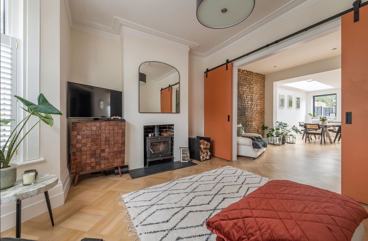 Living room with sliding doors opening into the kitchen. Exposed brickwork and warm tones, throws and rugs.