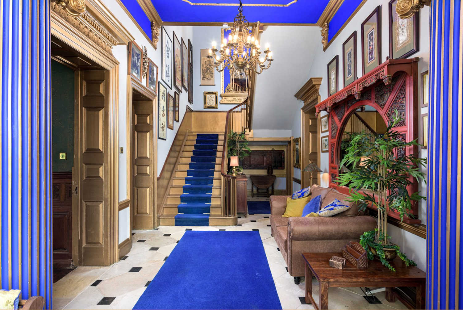 Opulent hallway with pillars painted in royal blue and gold, black and white marble tiles and a grand staircase