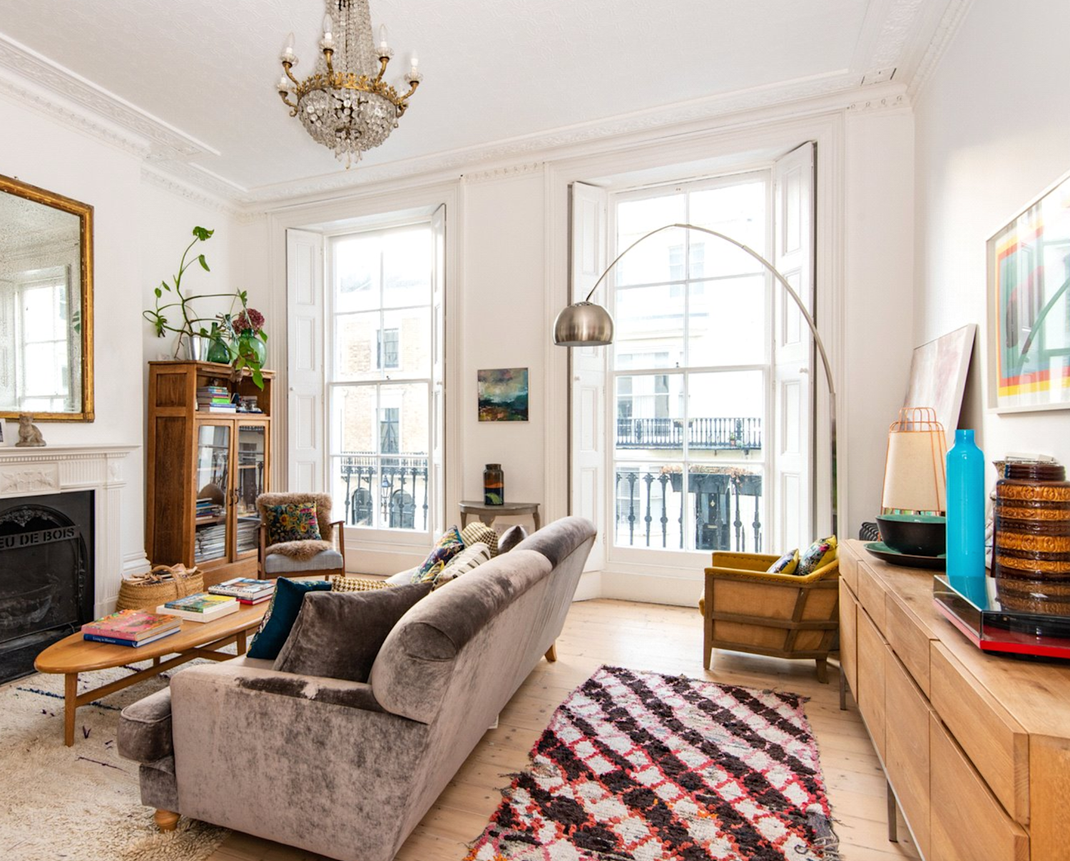 Interior of a Georgian townhouse living room, with exposed wood floor and modern furniture but original fireplace, windows and shutters