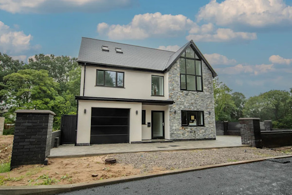 Exterior of an attractive 5-bed new-build home in Wales, featuring black window frames and white exterior cladding