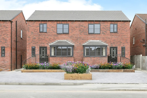 The exterior of a terraced new-build house with red brick and a large paved driveway