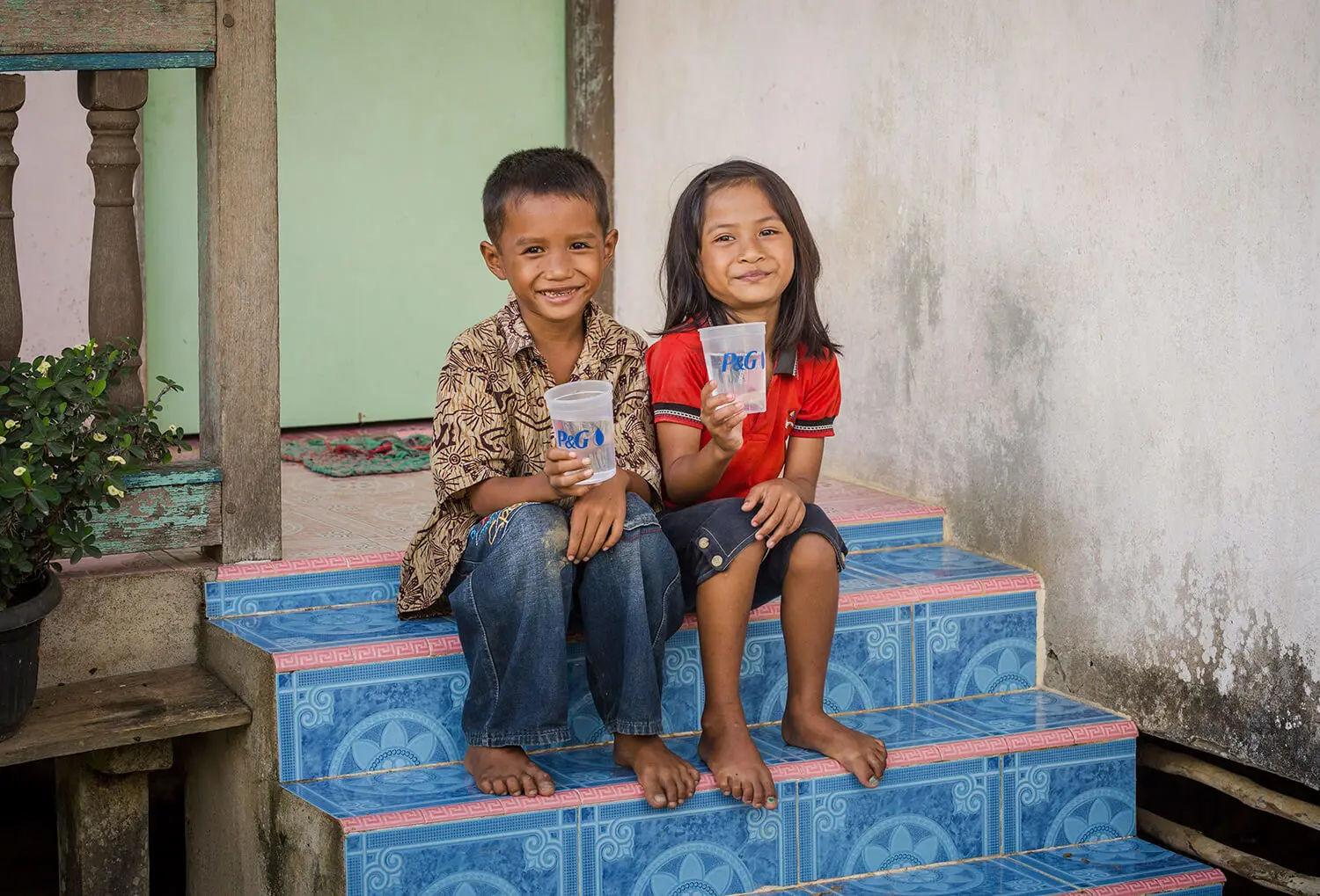 Crianças sorrindo e segurando um copo de água purificada