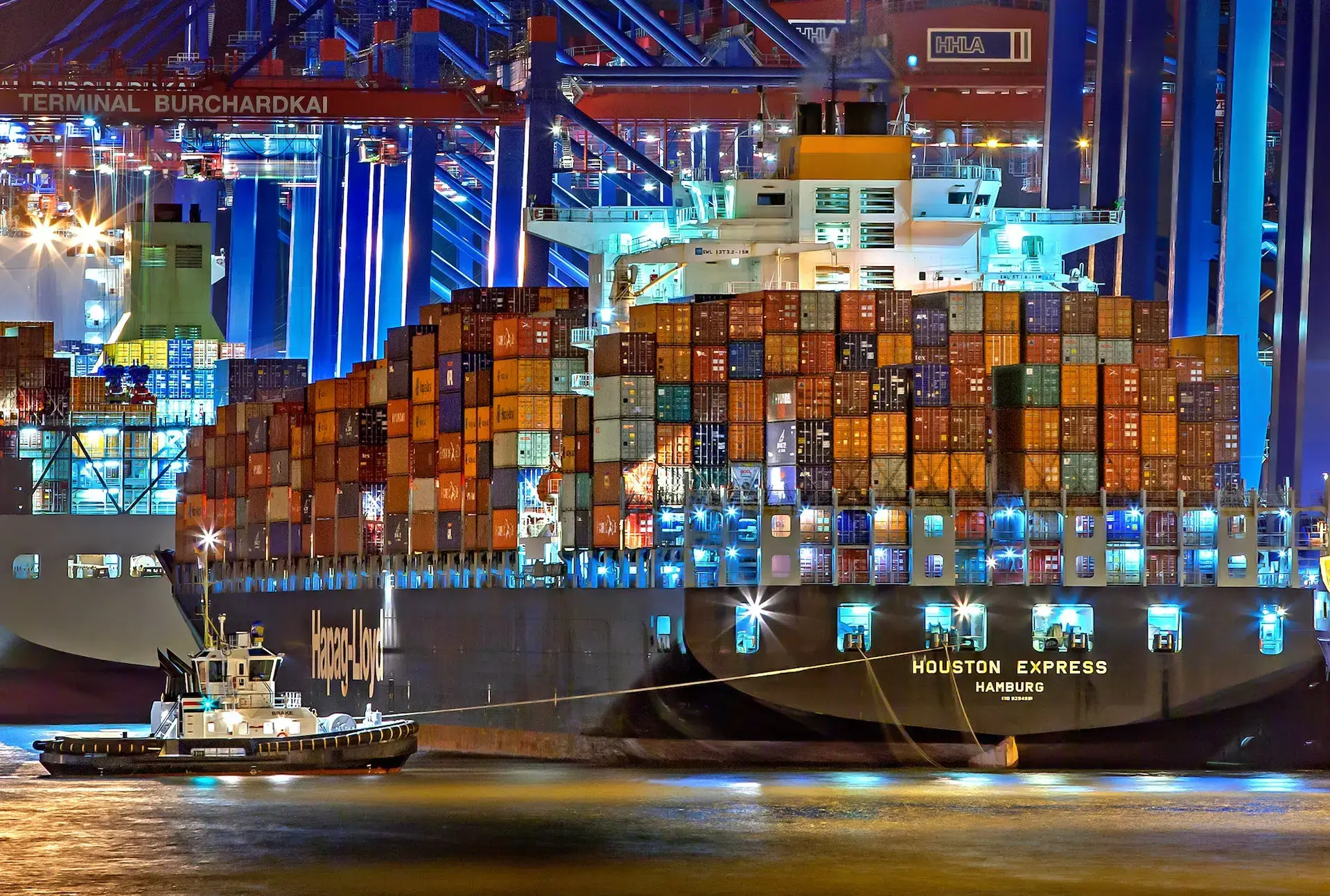 A large boat filled with shipping containers at a dock at night