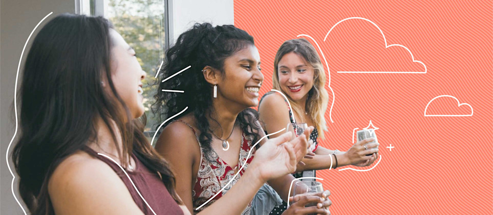 three female friends laughing on a balcony with a salmon-colored background