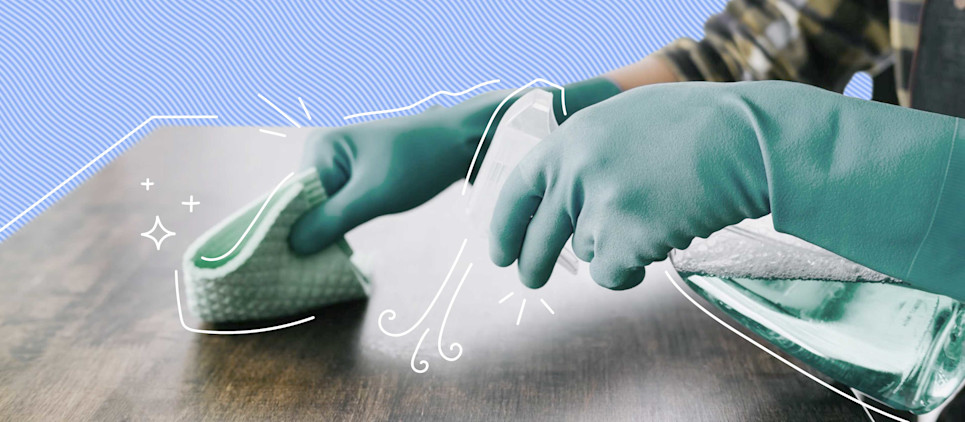 blue gloves wiping down wood table with sponge