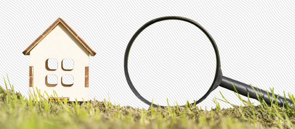 Magnifying glass sits next to miniature house figurine.
