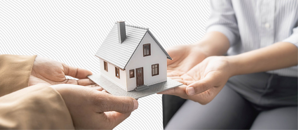 Two people's hands hold a miniature house figurine between them.