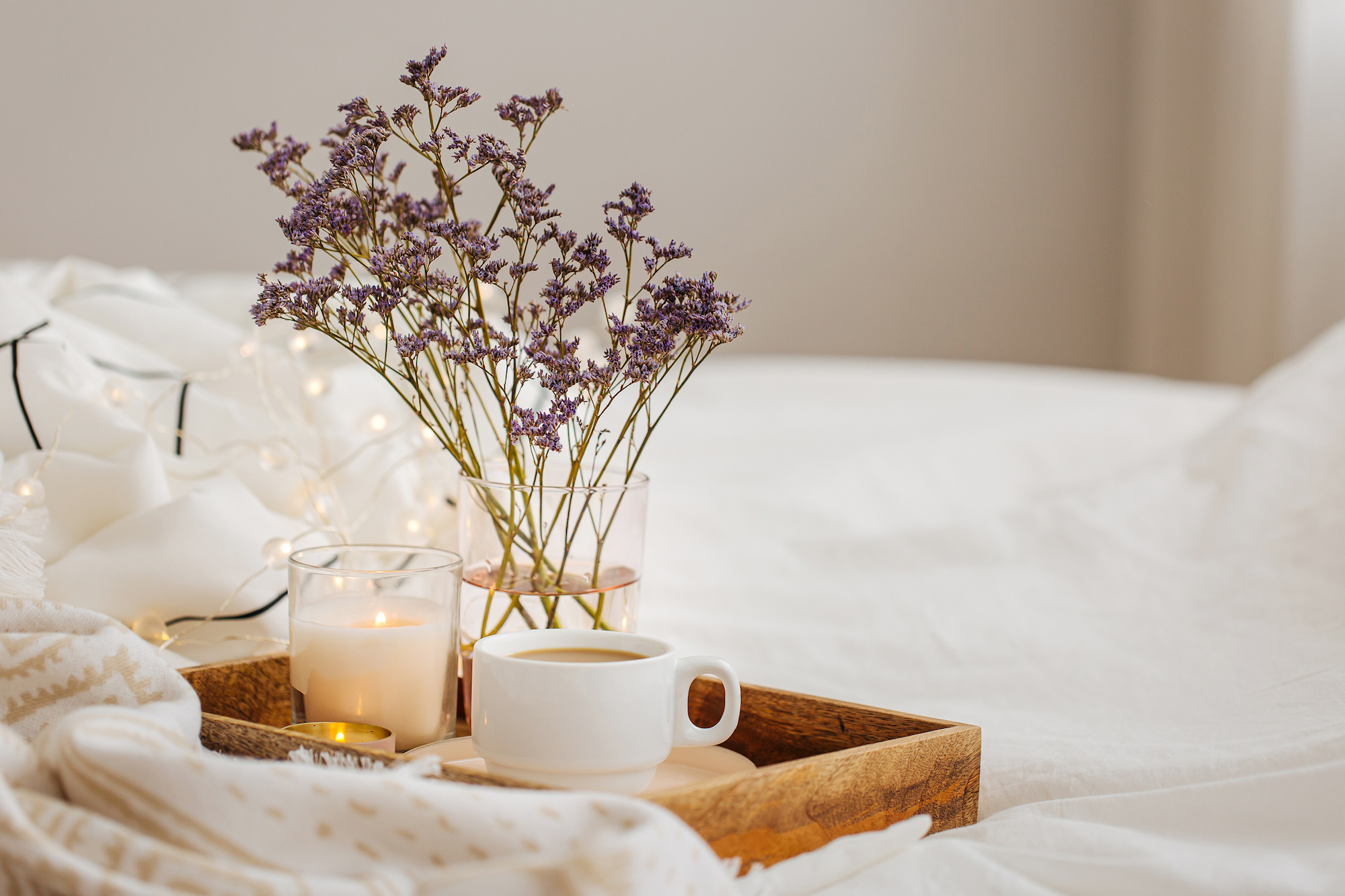 Tray set on a bed with a candle, flowers and a mug. 