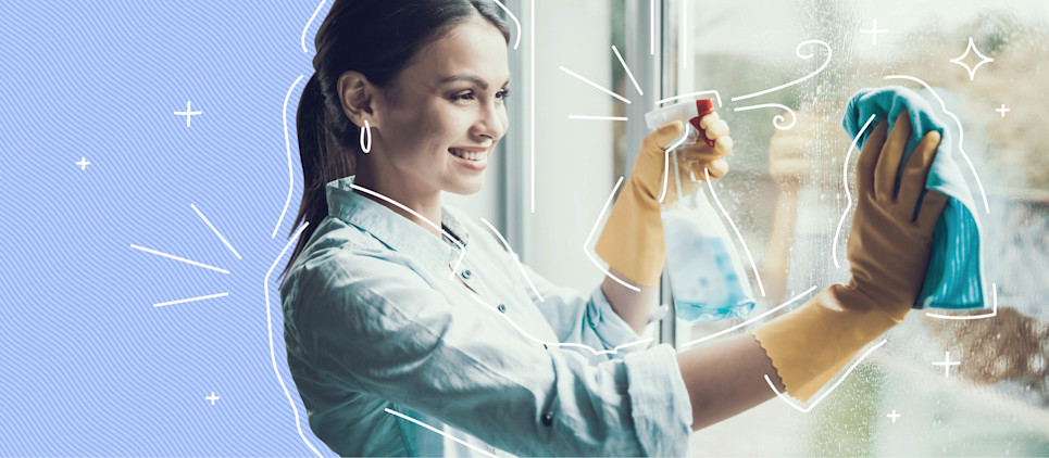 Woman wearing yellow gloves cleans a window with a cloth and spray bottle.