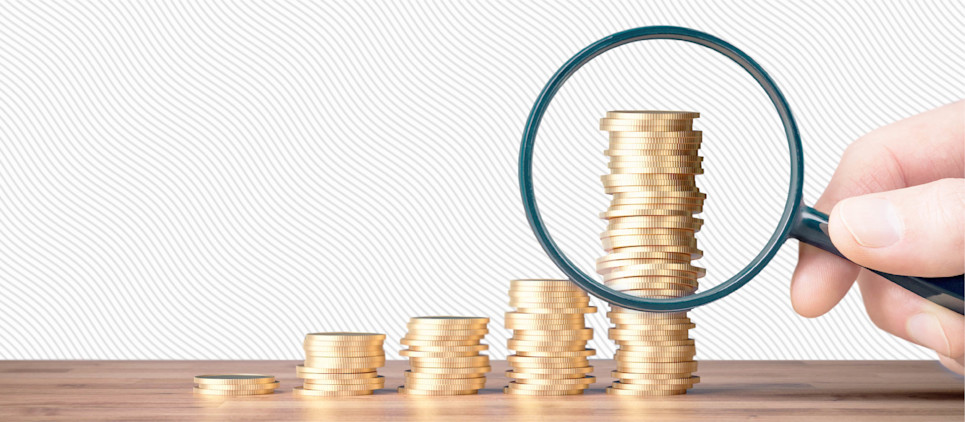 Stacks of coins and a magnifying glass examining the tallest stack. 