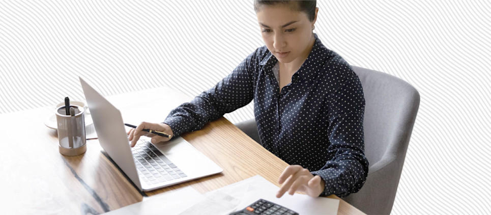 Woman sits at a desk with a laptop and a calculator.