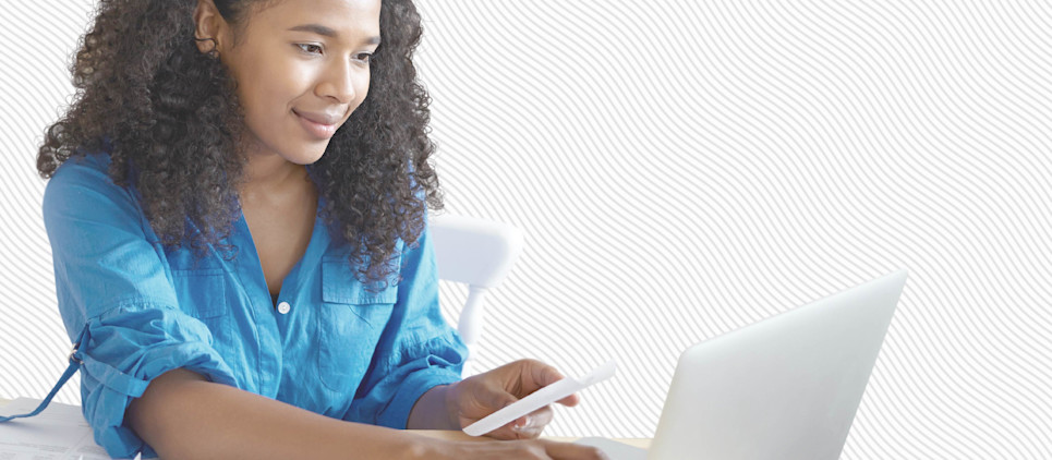 Woman sits in front of her laptop holding her cell phone.