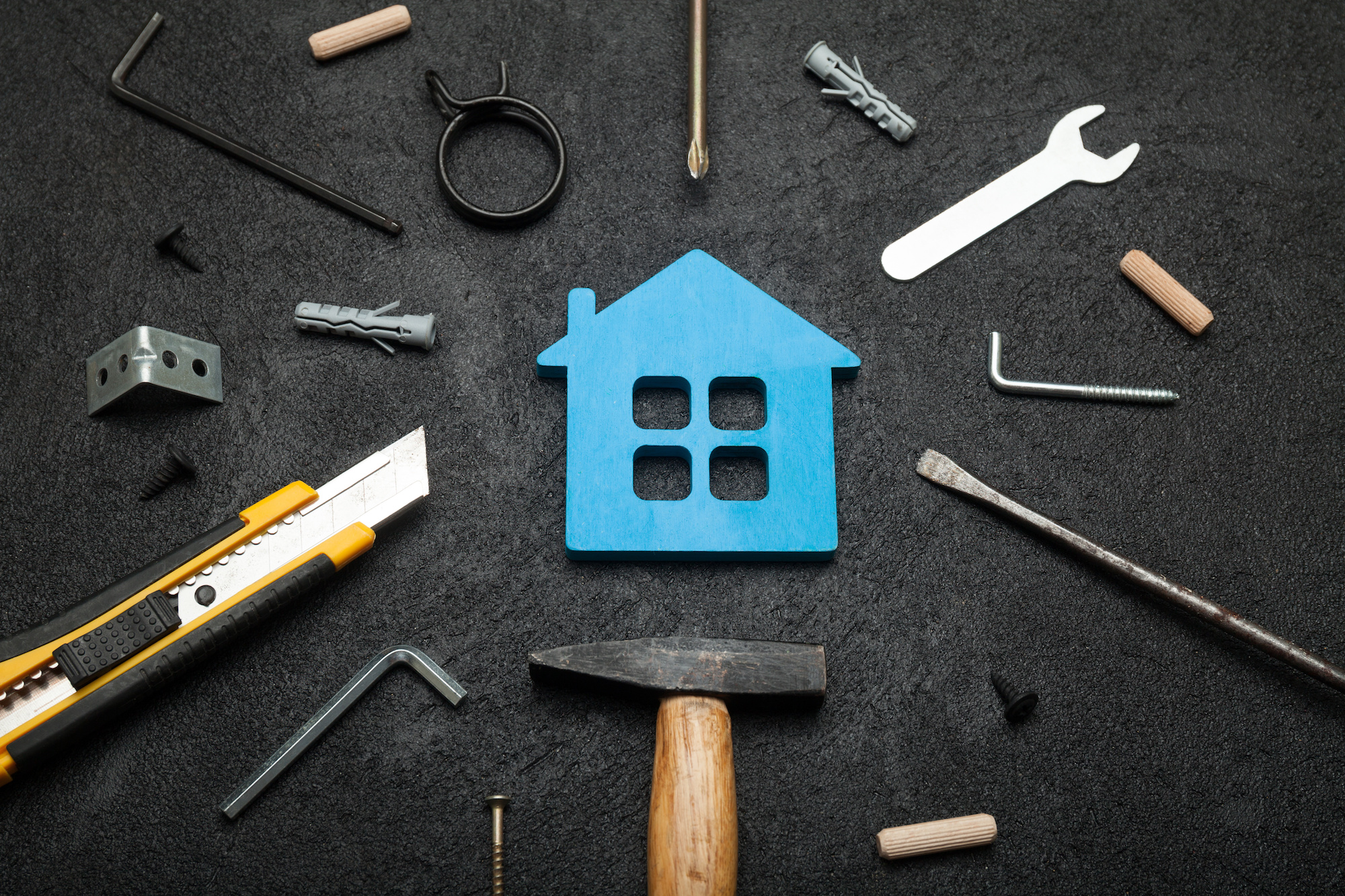 Different tools surround a blue cut out house figurine. 