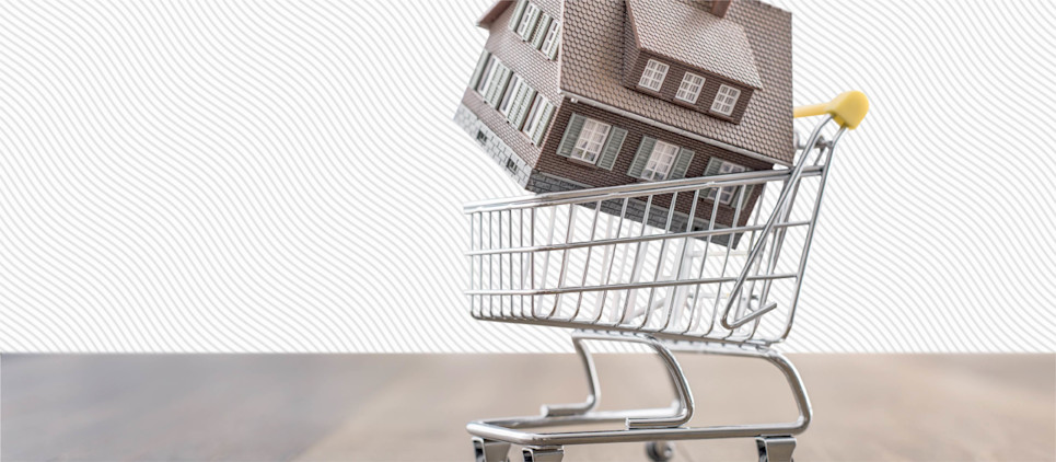 Miniature house figurine sits in a miniature shopping cart.