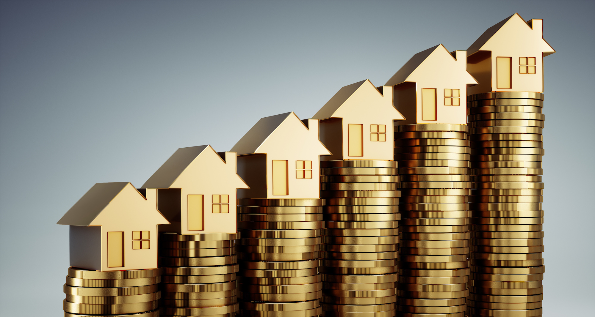 Miniature gold houses sit on stacks of gold coins. 
