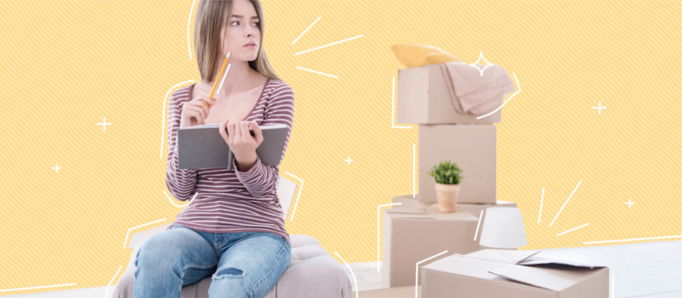 Woman holds a clipboard sitting on top of a box with a pile of boxes next to her.