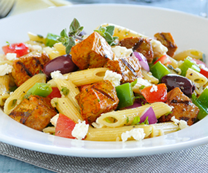 Greek salad penne in white plate on grey mat