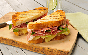 Sandwich on a wooden board made with white bread, cold cuts and cheese