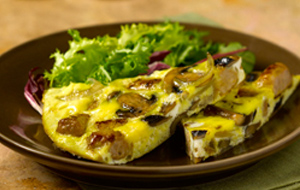 slice of frittata with sausages onion and mushrooms on brown plate with salad