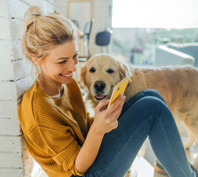 Woman updates benefits selections on mobile device and re-elects her flex spending account while her dog cheers her on.