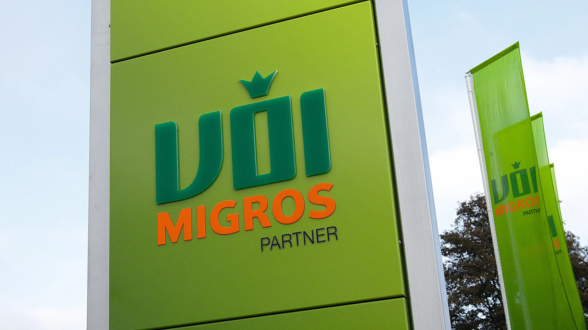VOI Migros-Partner Logo mit VOI Migros-Partner Fahnen im Hintergrund