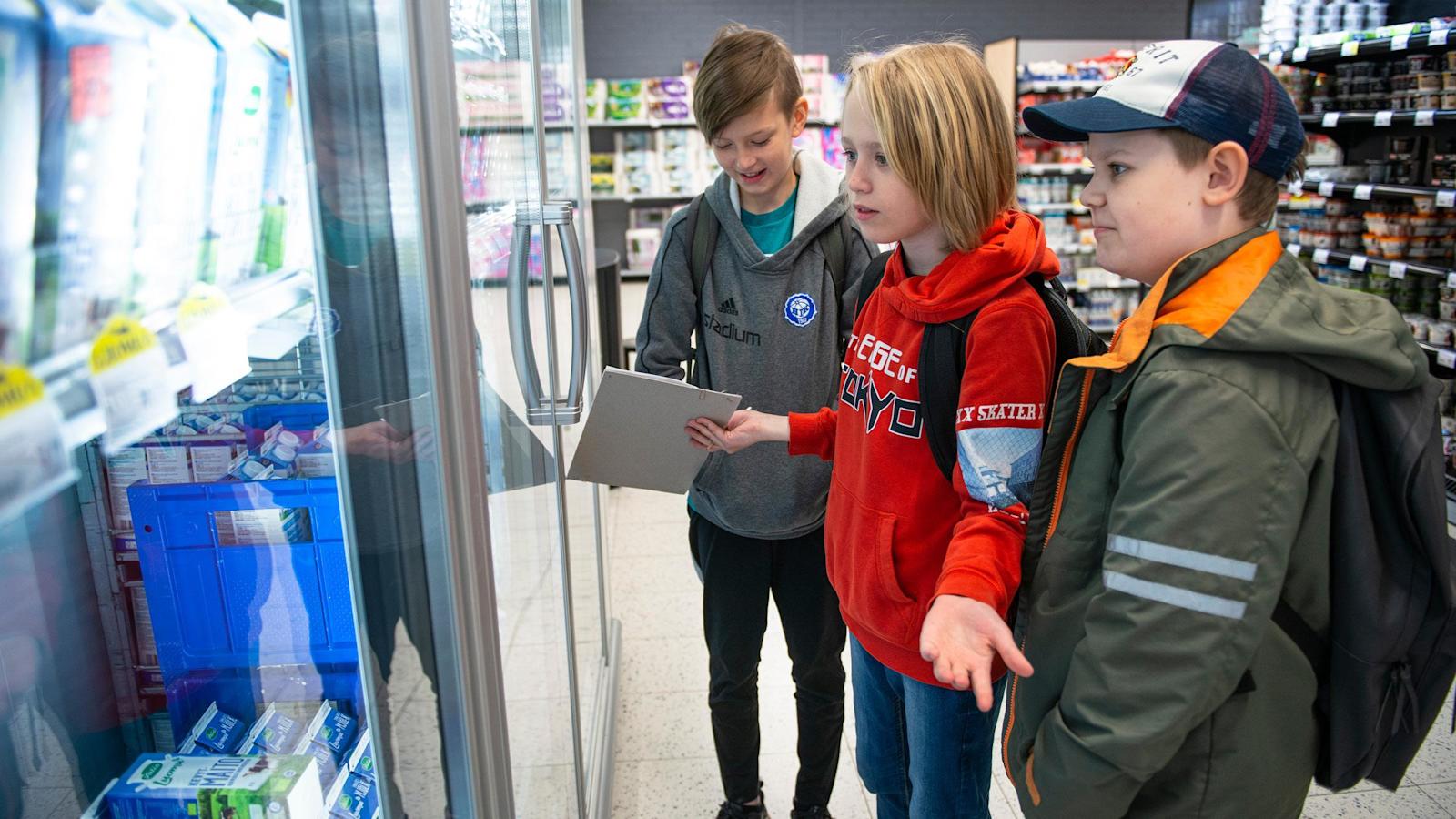 Leo Kondo, Amos Arponen ja Rex Nyberg vertailevat hintoja maitohyllyllä Vallilan S-marketissa.