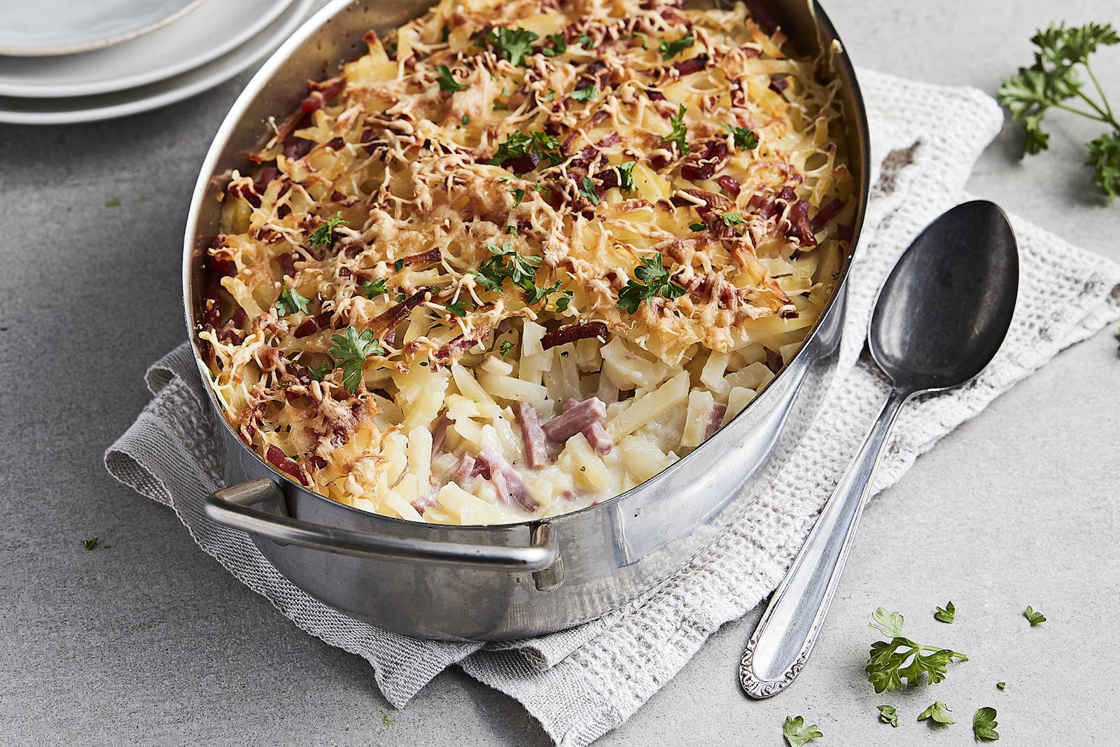 Helppo kinkkukiusaus metallisessa vuoassa, jonka alla harmaa liina ja vieressä metallinen tarjoilulusikka.