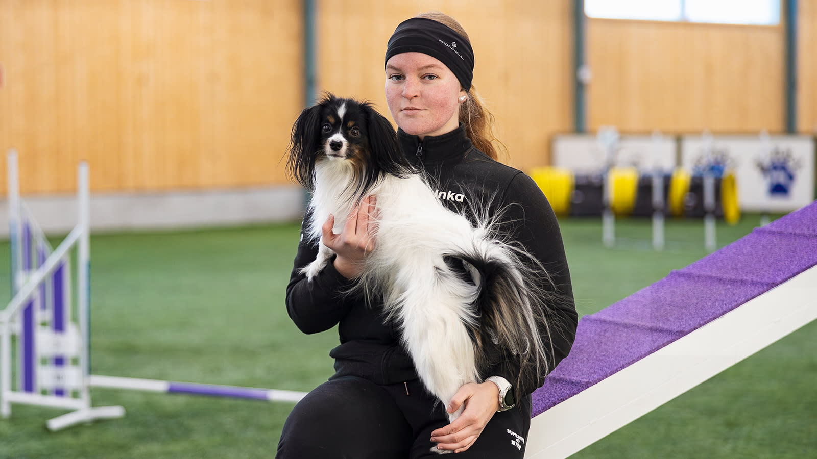 Inka Eerola poseeraa agilityradalla Jeti-koira sylissään.