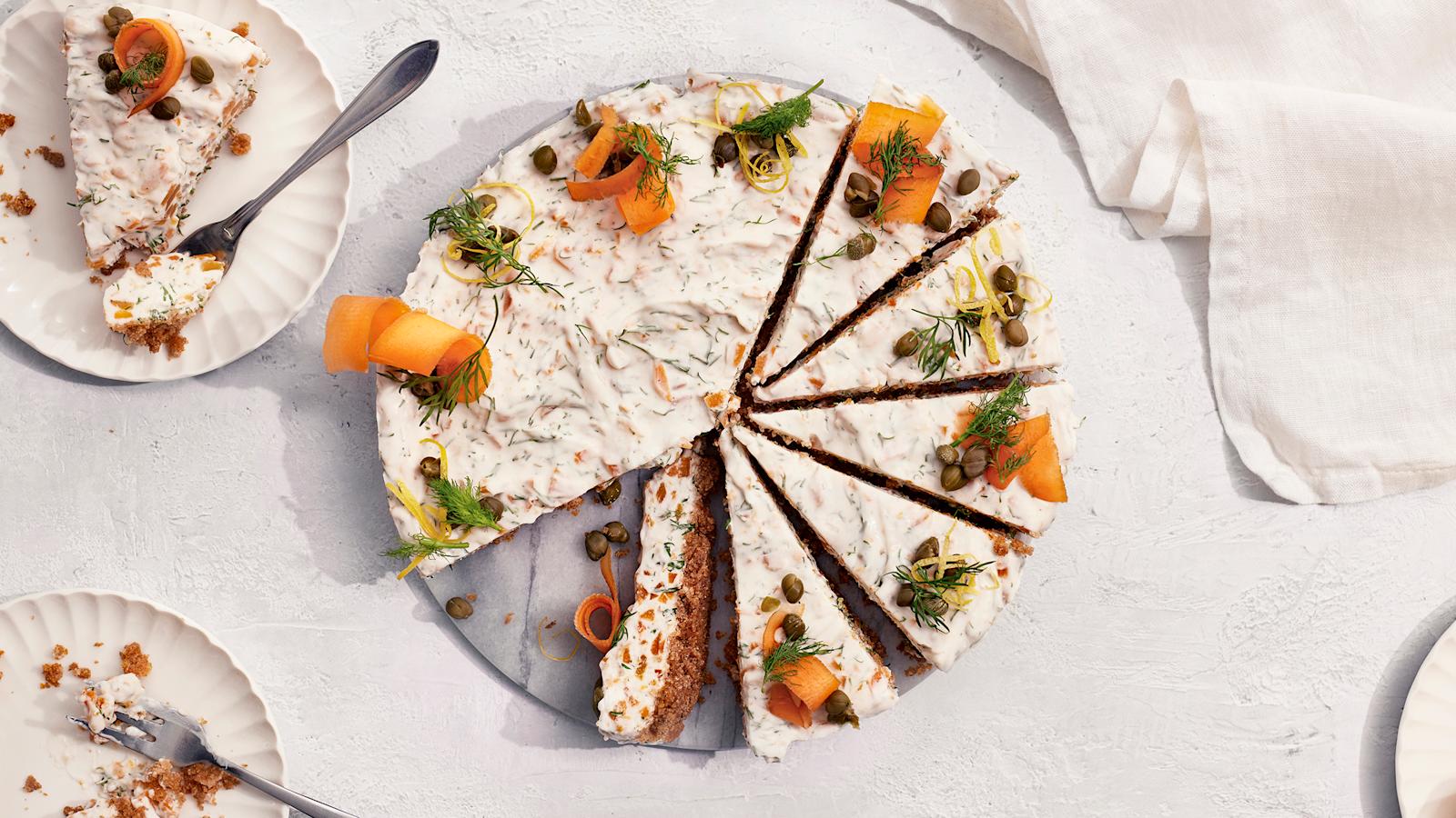 Vegaaninen kylmäsavulohijuustokakku, josta on leikattu useita paloja valmiiksi tarjoilulautaselle. Vieressä kaksi lautasta, joilla kakkupalat ja leivoshaarukat.