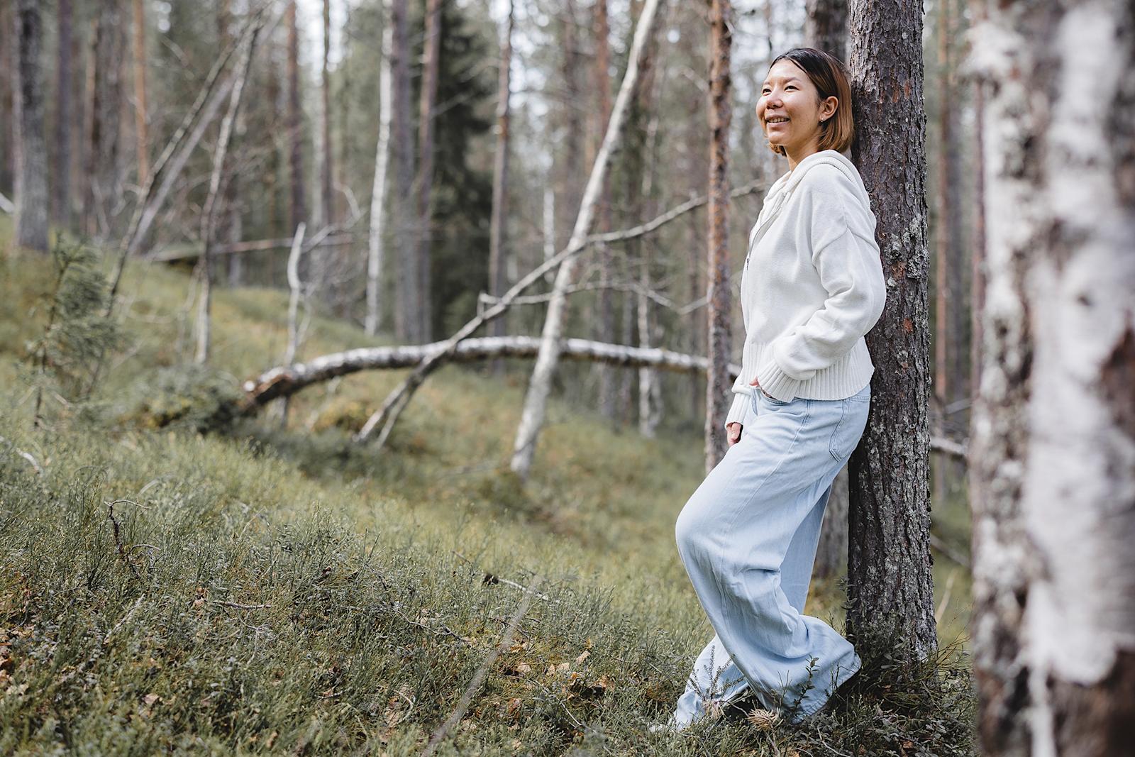 Nainen nojaa metsässä puuhun