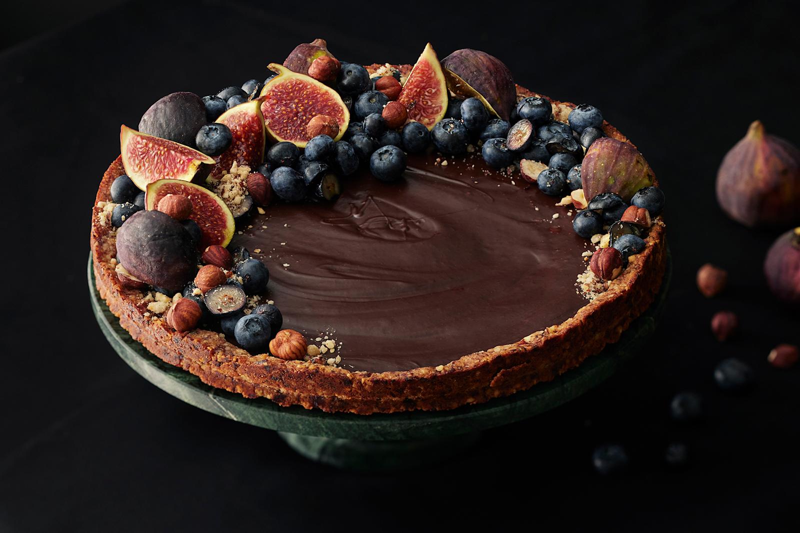 Vegaaninen suklaatorttu, joka koristeltu tuoreilla viikunoilla, pensasmustikoilla ja hasselpähkinöillä.