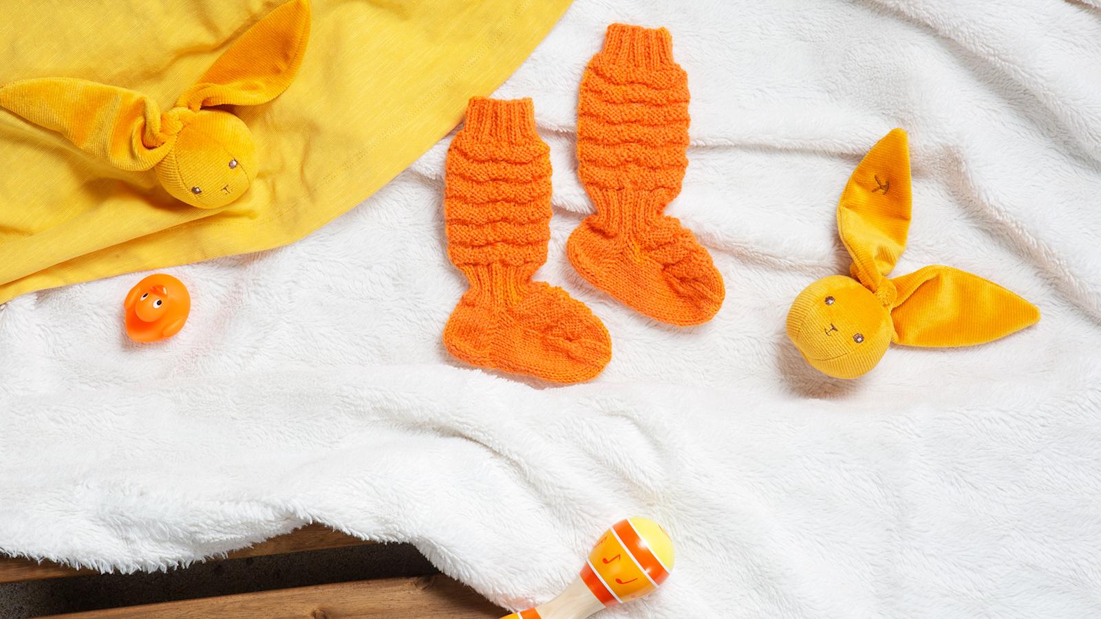 Oranssit vauvan villasukat valkoisen viltin päällä.